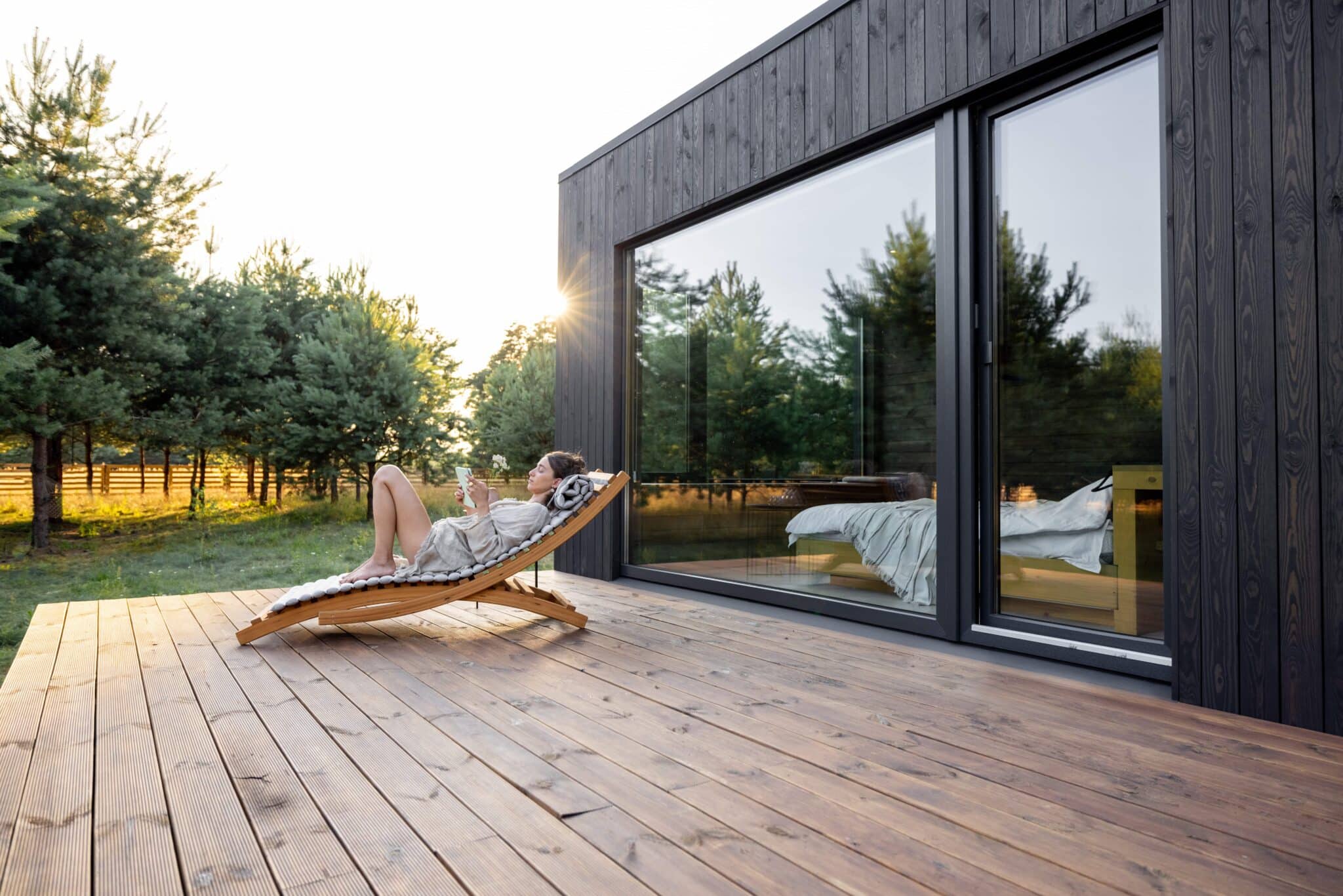 Woman sitting on a deck outside a home exterior with large window