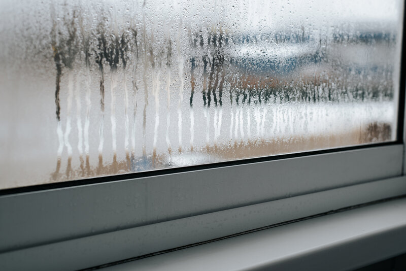 Foggy window pane with condensation indicating a failed seal in an old home